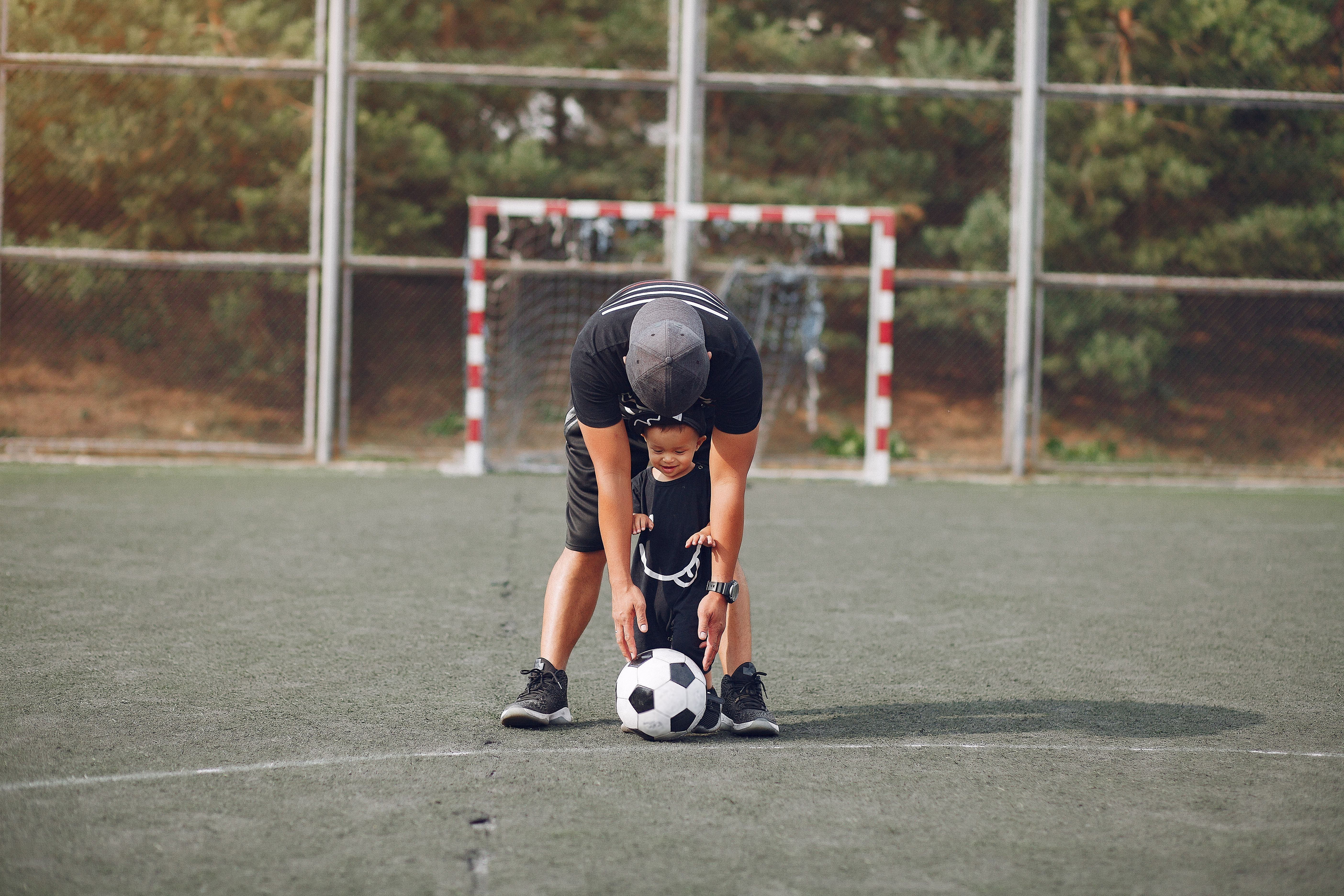 Young player bent over football on training pitch, goal behind