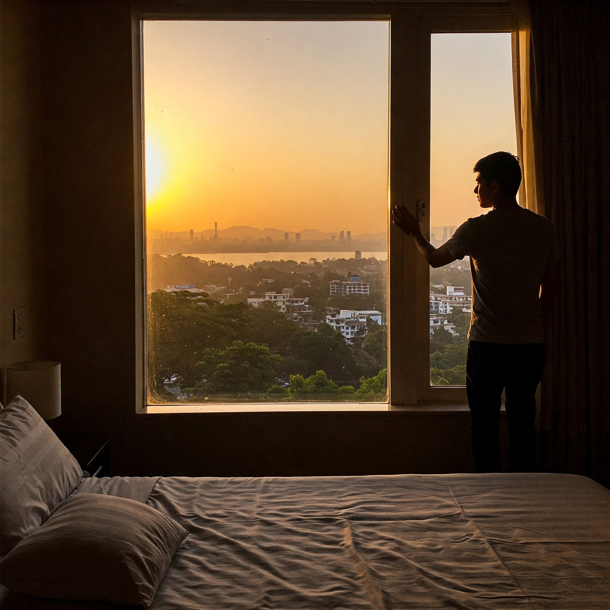 Person opening curtains onto a city skyline at sunrise