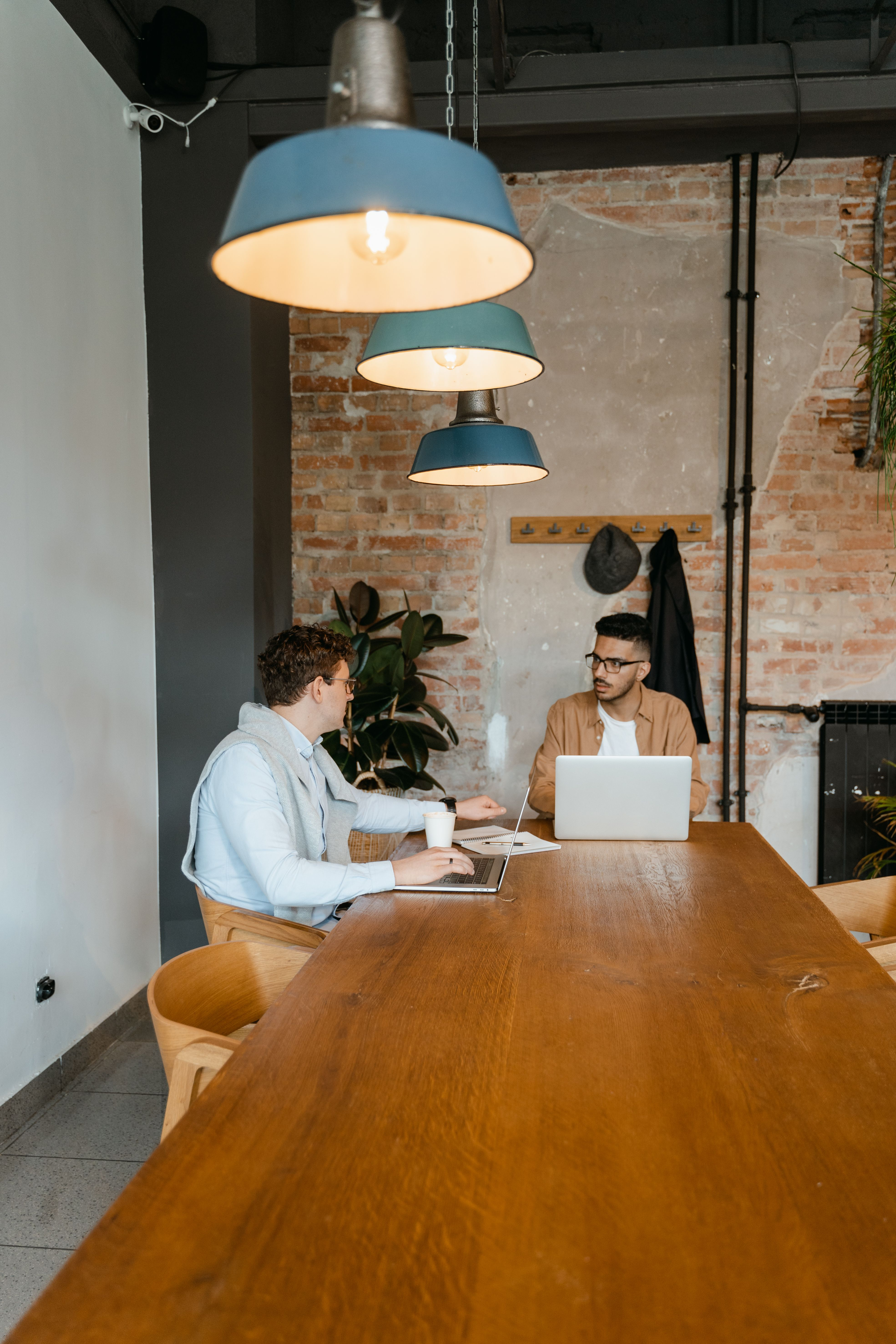 Two people working at a laptop in a brick-walled café