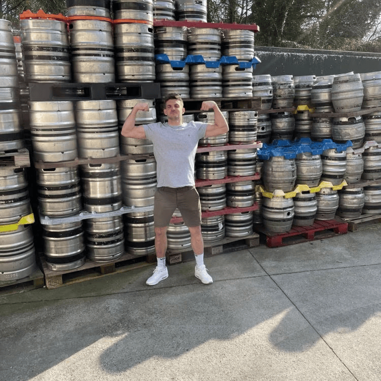 Person standing among stacked beer kegs in a brewery