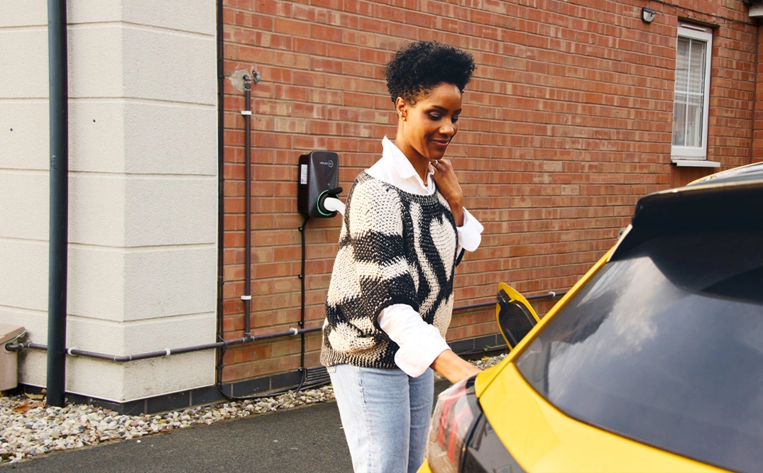 Woman charging an electric vehicle at a home EV charger, highlighting clean energy and sustainable transport