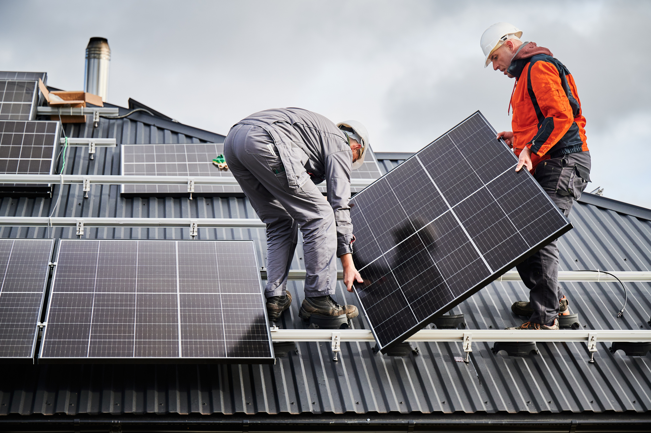 Technicians carrying photovoltaic solar module while installing solar panel system on roof of house