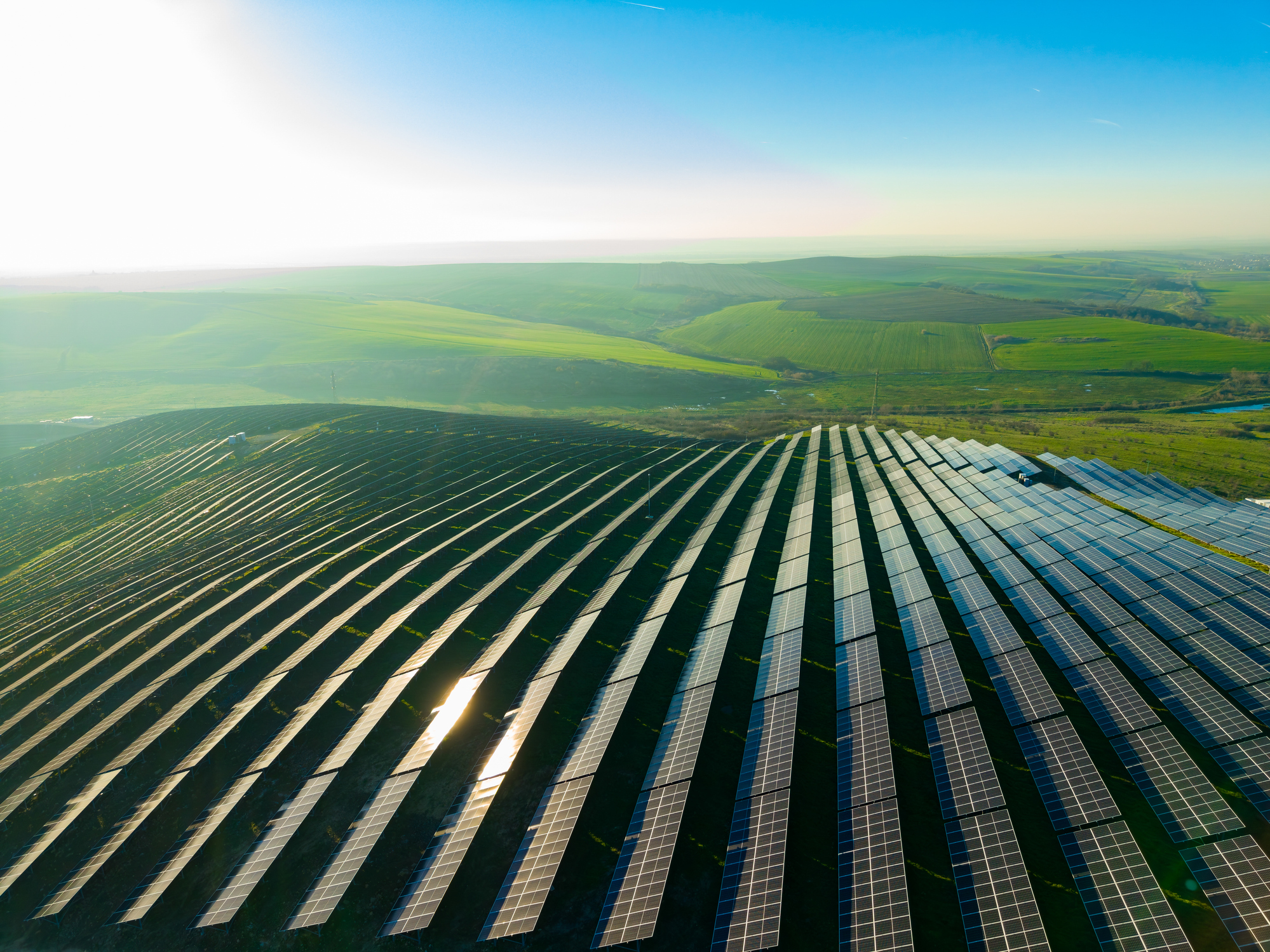 Solar panels cover the hills of a vast landscape with green fields during a bright day