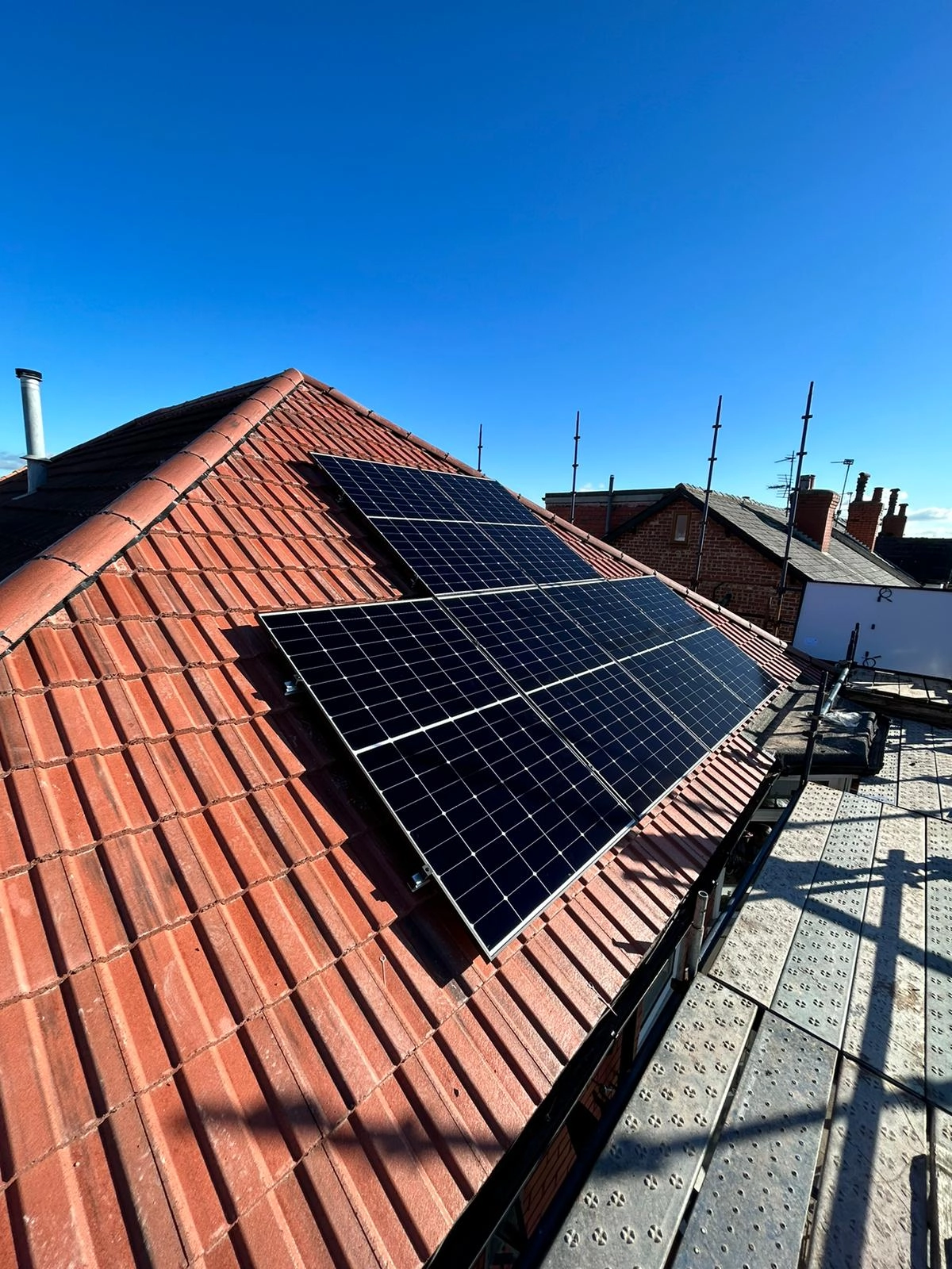 Solar panels installed on a red tiled residential roof under clear blue sky generating renewable energy