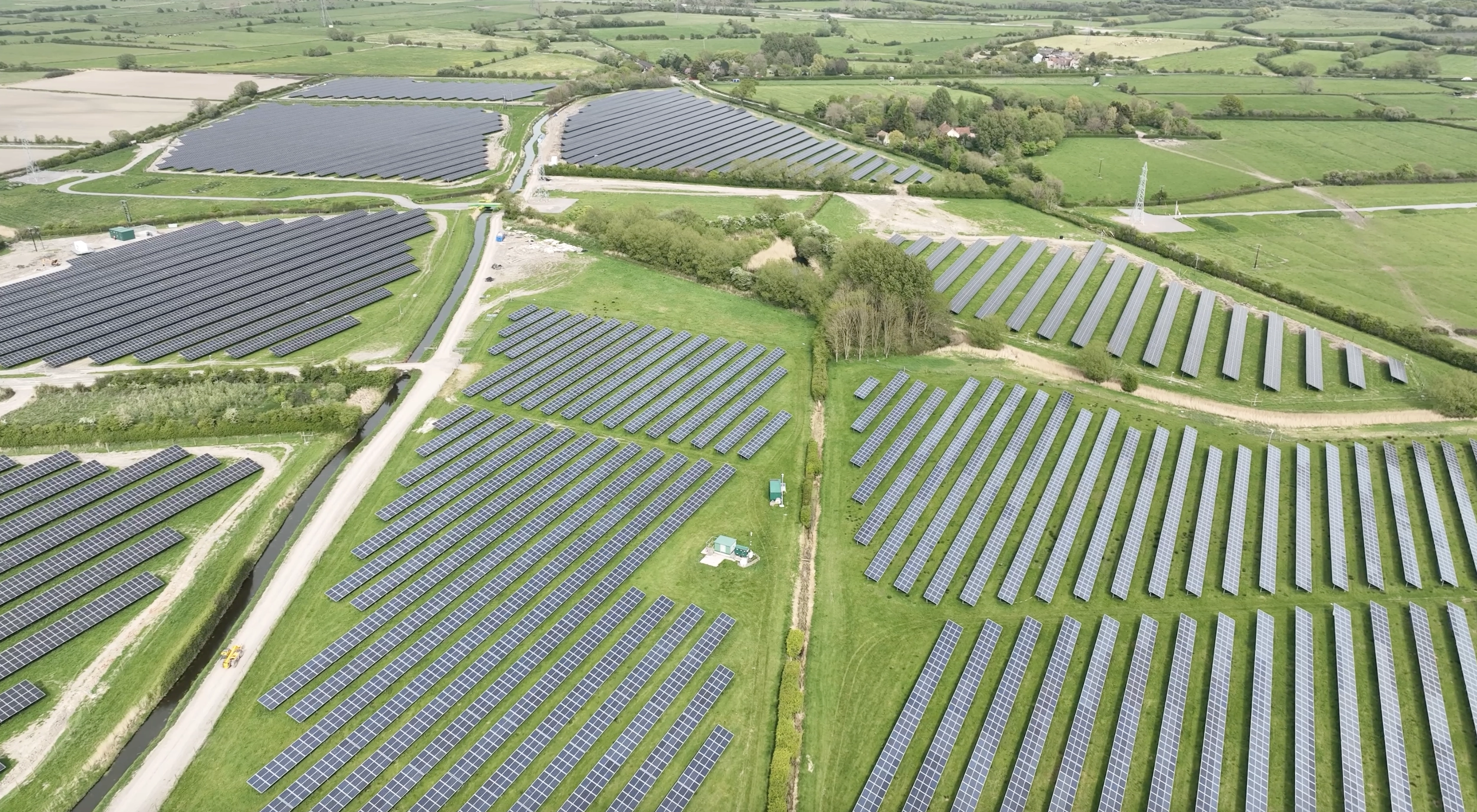 Aerial view of large solar farm with multiple fields of photovoltaic panels generating renewable energy in rural landscape