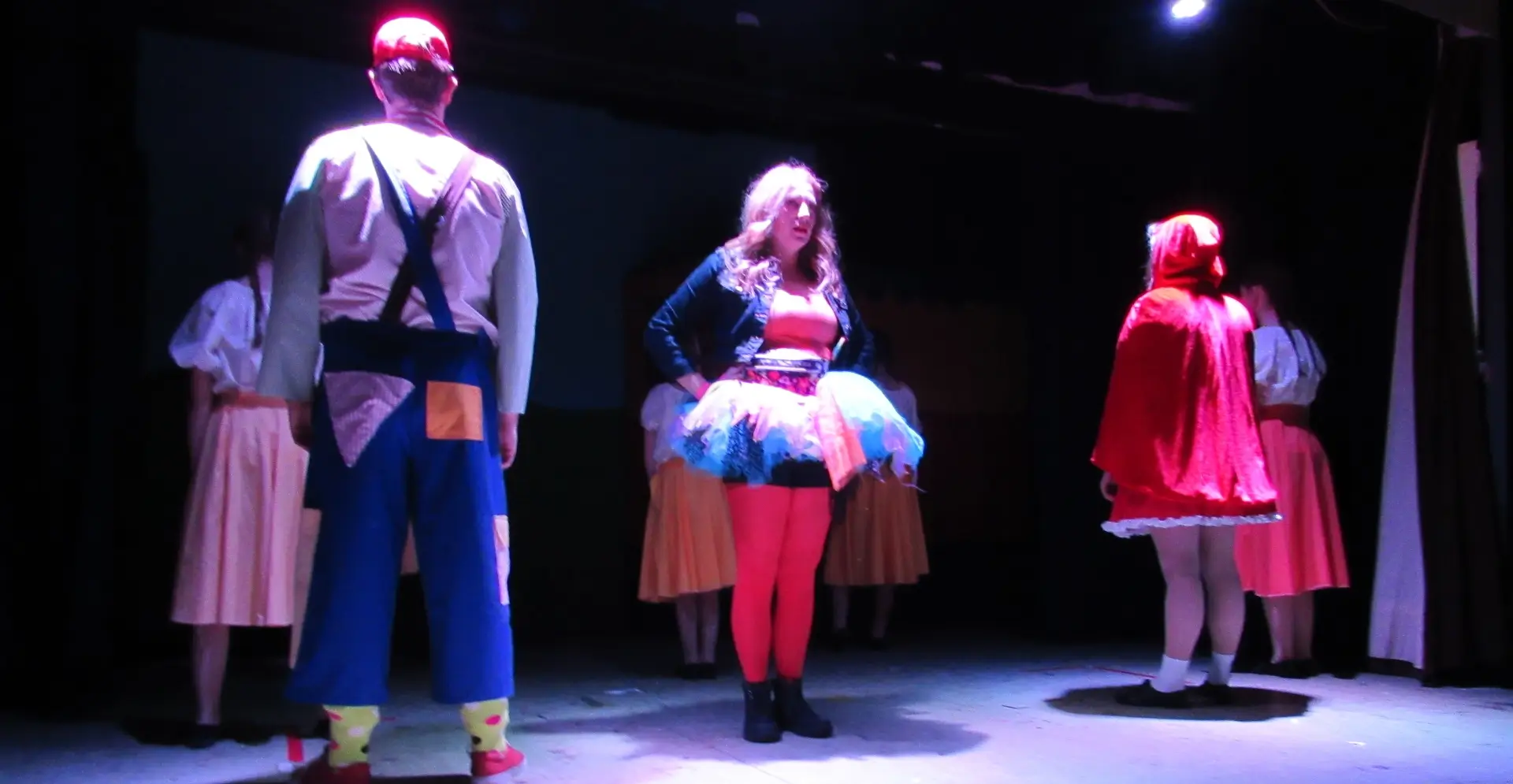 Three performers on stage, village idiot with back turned, fairy facing front and little red riding hood facing the back